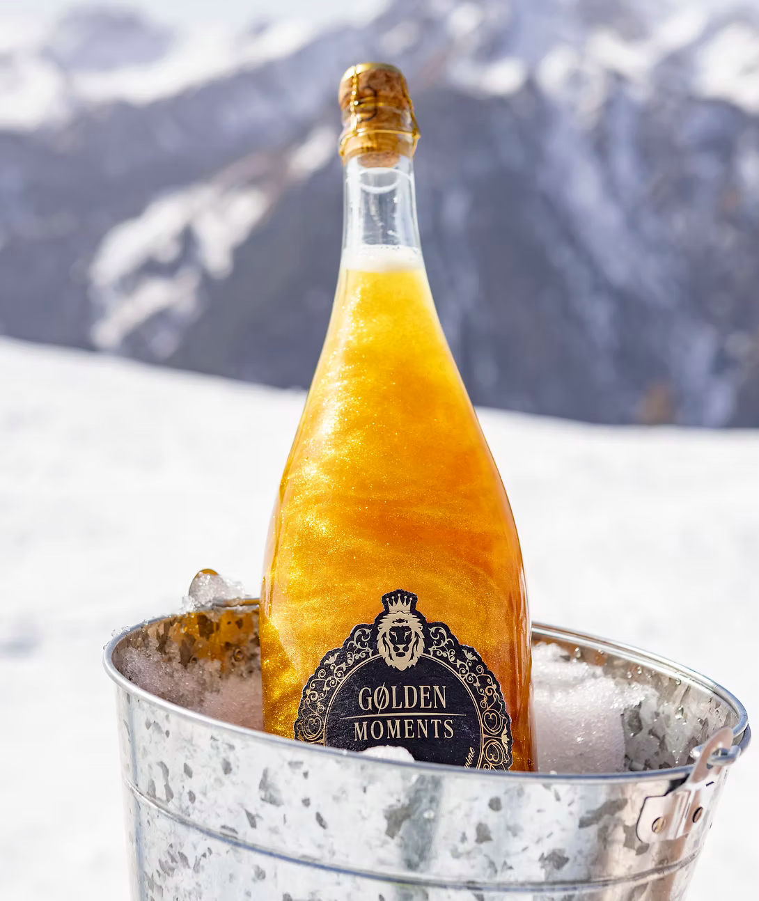 Golden Moments Sparkling Wine mit goldenem Schimmer im Eiskübel vor winterlicher Bergkulisse